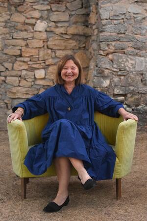 Bild vergr&ouml;&szlig;ern: Eine Frau in einem dunkelblauen Kleid sitzt auf einem gelben Sofa.