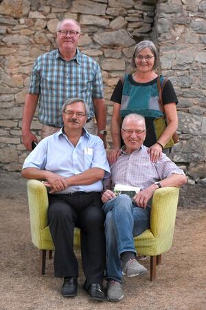 Bild vergr&ouml;&szlig;ern: Zwei Männer sitzen auf einem gelben Sofa und ein Mann und eine Frau stehen hinter ihnen.