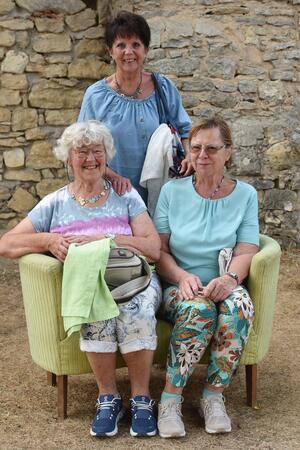 Bild vergr&ouml;&szlig;ern: Zwei Frauen sitzen auf einem gelben Sofa und eine Frau steht dahinter.