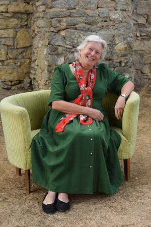 Bild vergr&ouml;&szlig;ern: Eine Frau im grünen Kleid sitzt auf einem gelben Sofa.